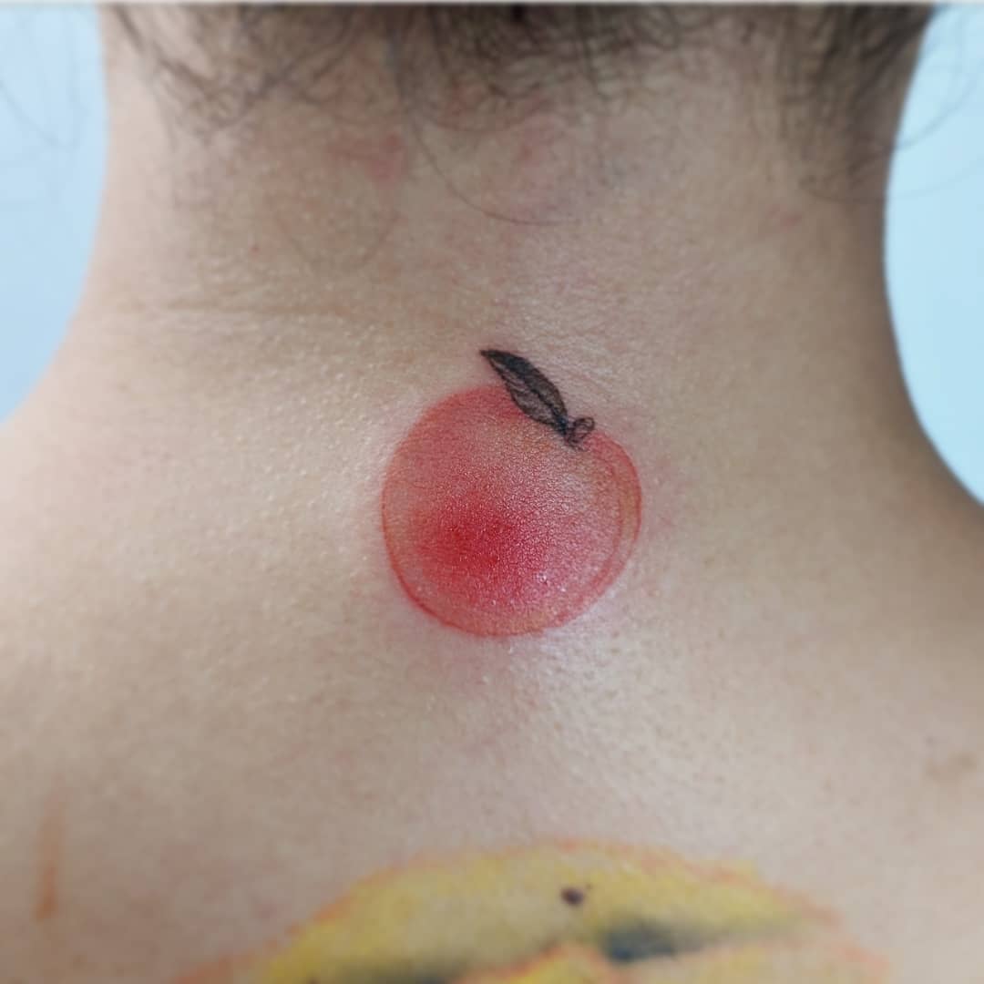 Small peach tattoo with a single leaf on the back of a neck